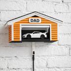 Orange mailbox with a car graphic and 'DAD' label on a white brick wall.